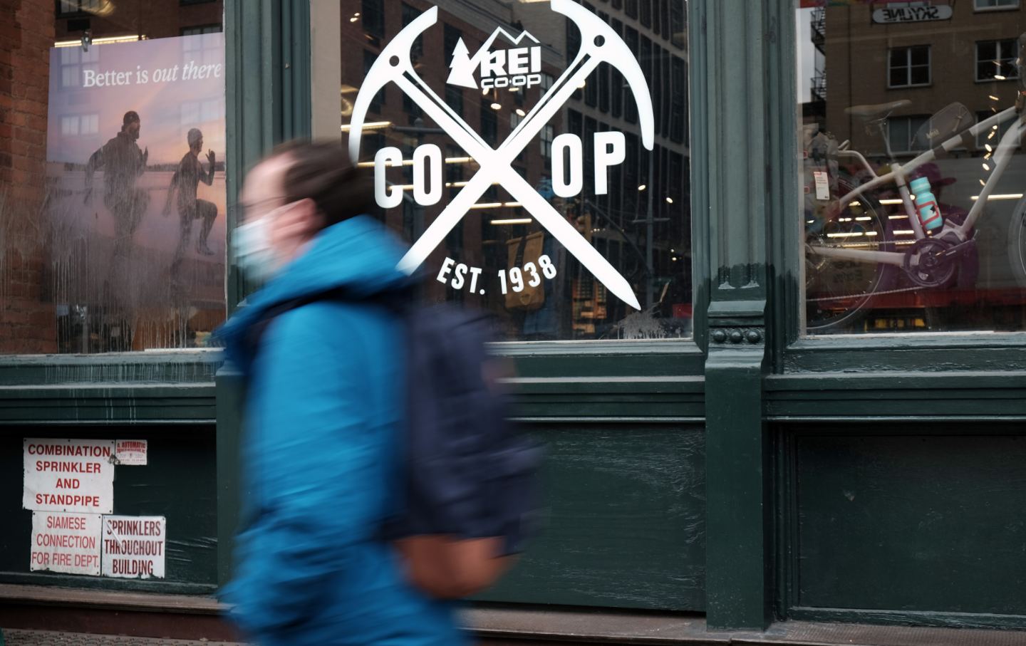 A man walks past a shop window with the REI logo on it,