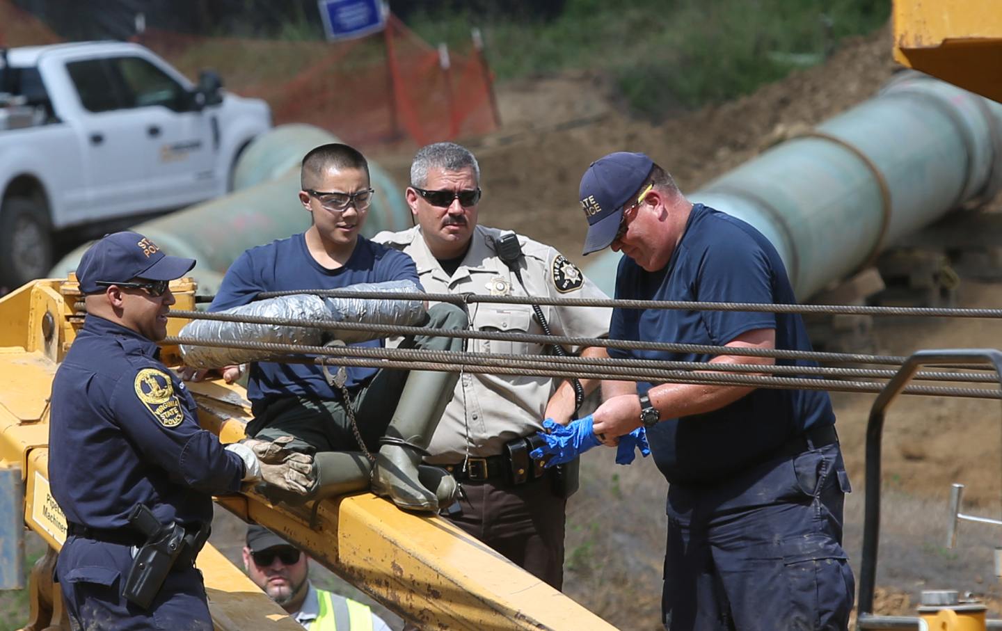 Several police officers surround a person whose hands are wrapped around a piece of construction equipment.