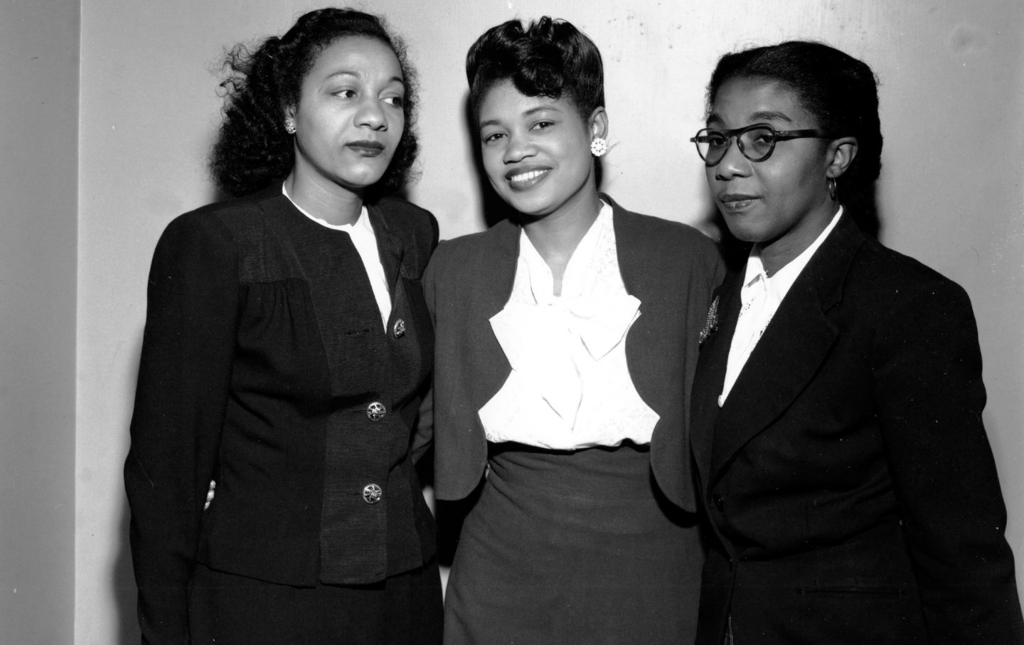 Three Black women in formal dress pose for a photo