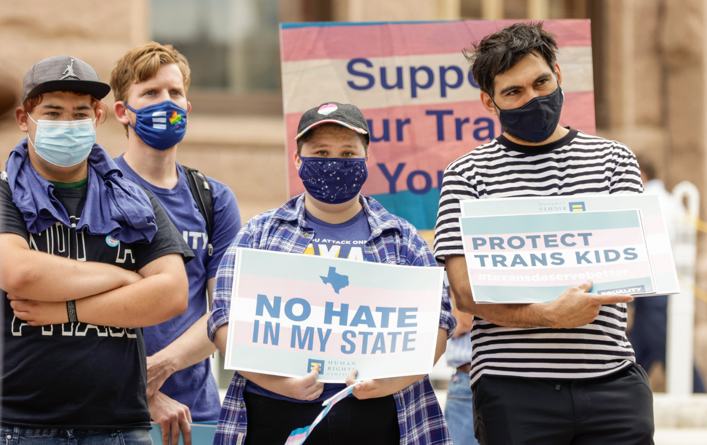 Four protesters hold signs in favor of trans youth.