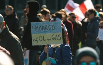 A person holds a sign the colors of the Ukranian flag with a slogan about an embargo of oil and gas