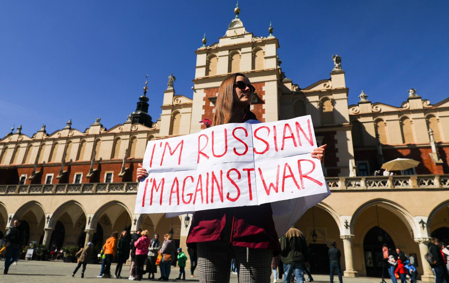 A woman stands in front of a building holding a sign