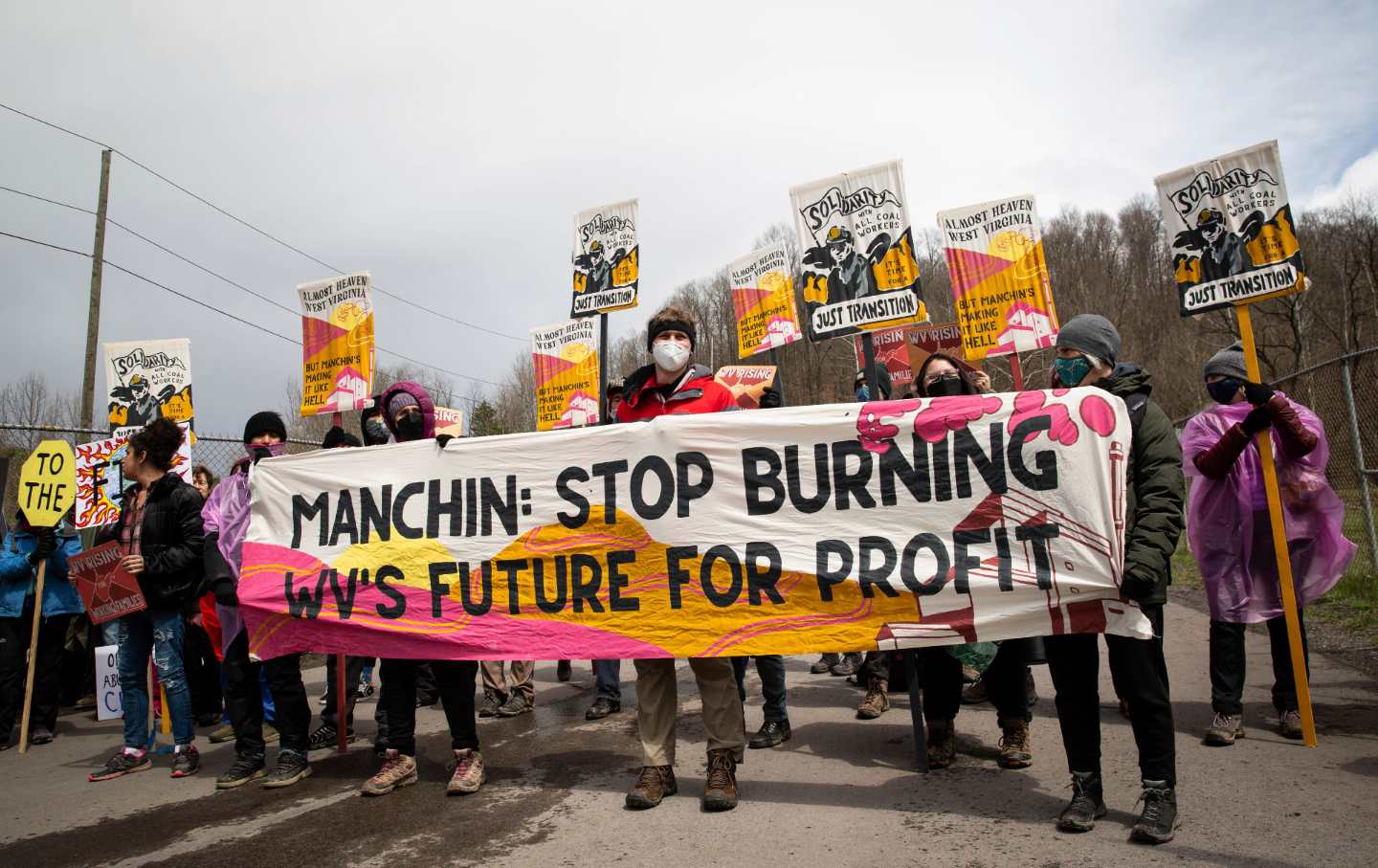 Protesters stand with a banner and signs about clean energy