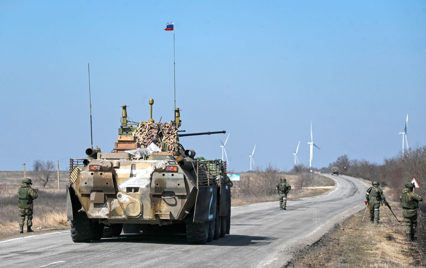 A tank on a road, with scattered soldiers walking alongside it.