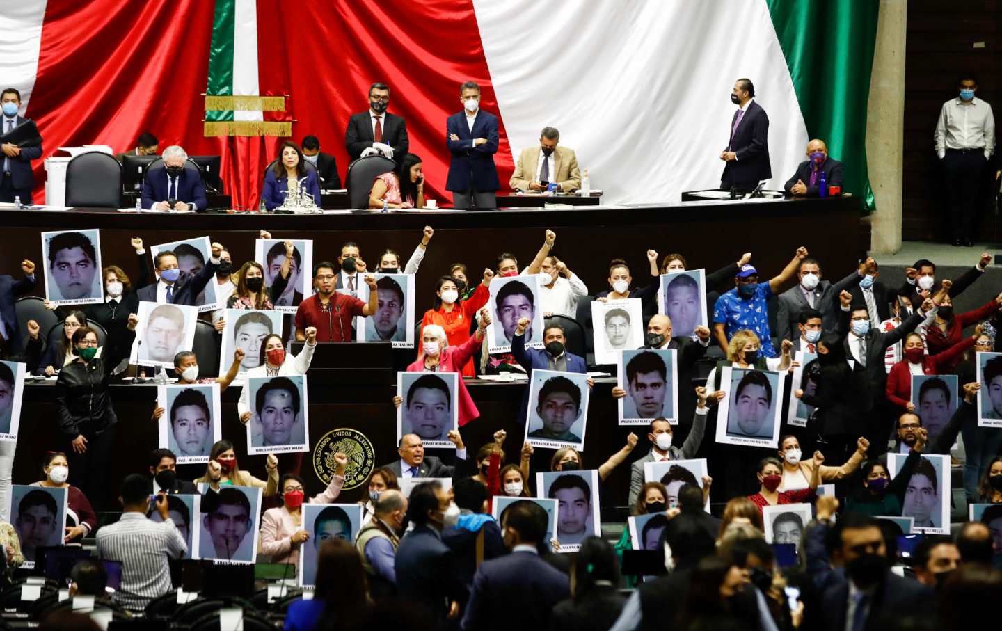 People in suits and masks holding head shots of students raise their fists.