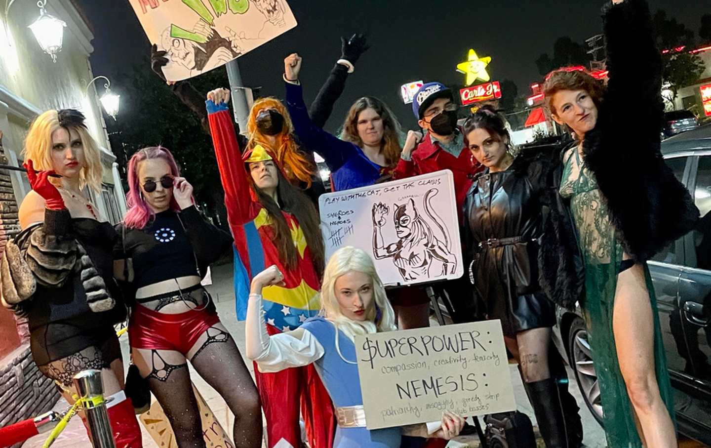 A group of women in costume hold signs. One raises her fist.