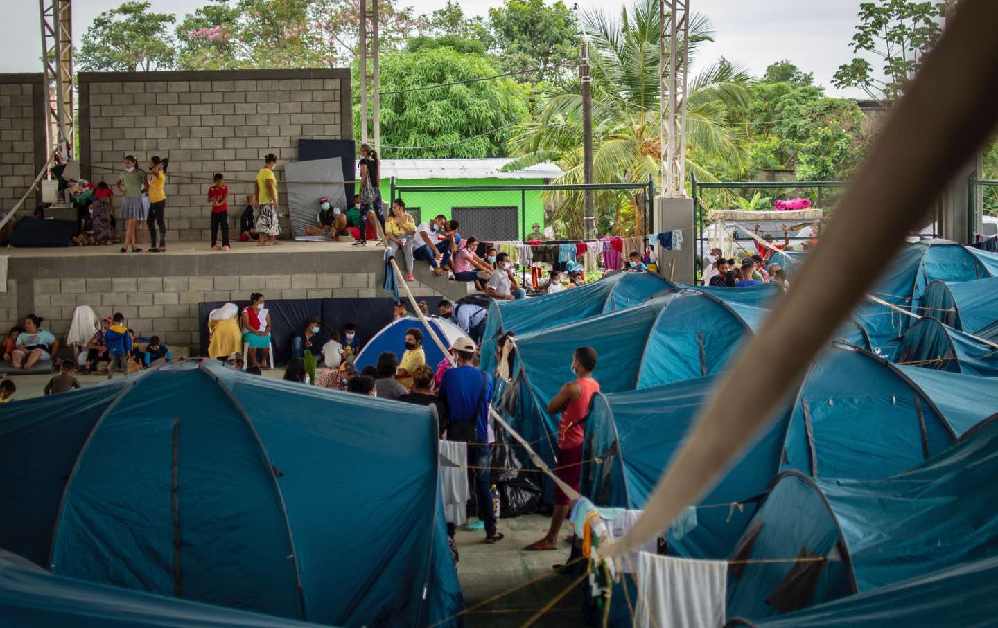 Uniform blue tents and hanging laundry and a crowd of people in a concrete shelter