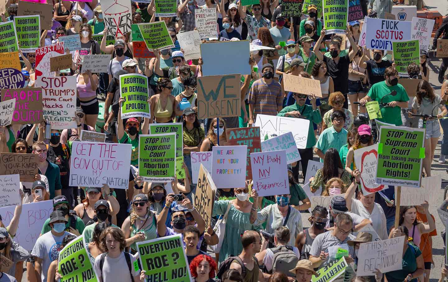 A crowd of people hold signs protesting the Supreme Court's decision to take away abortion rights.