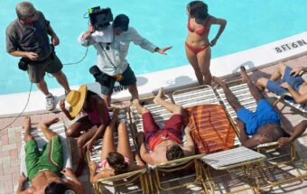 Group of adults lying by poolside, film crew giving instructions