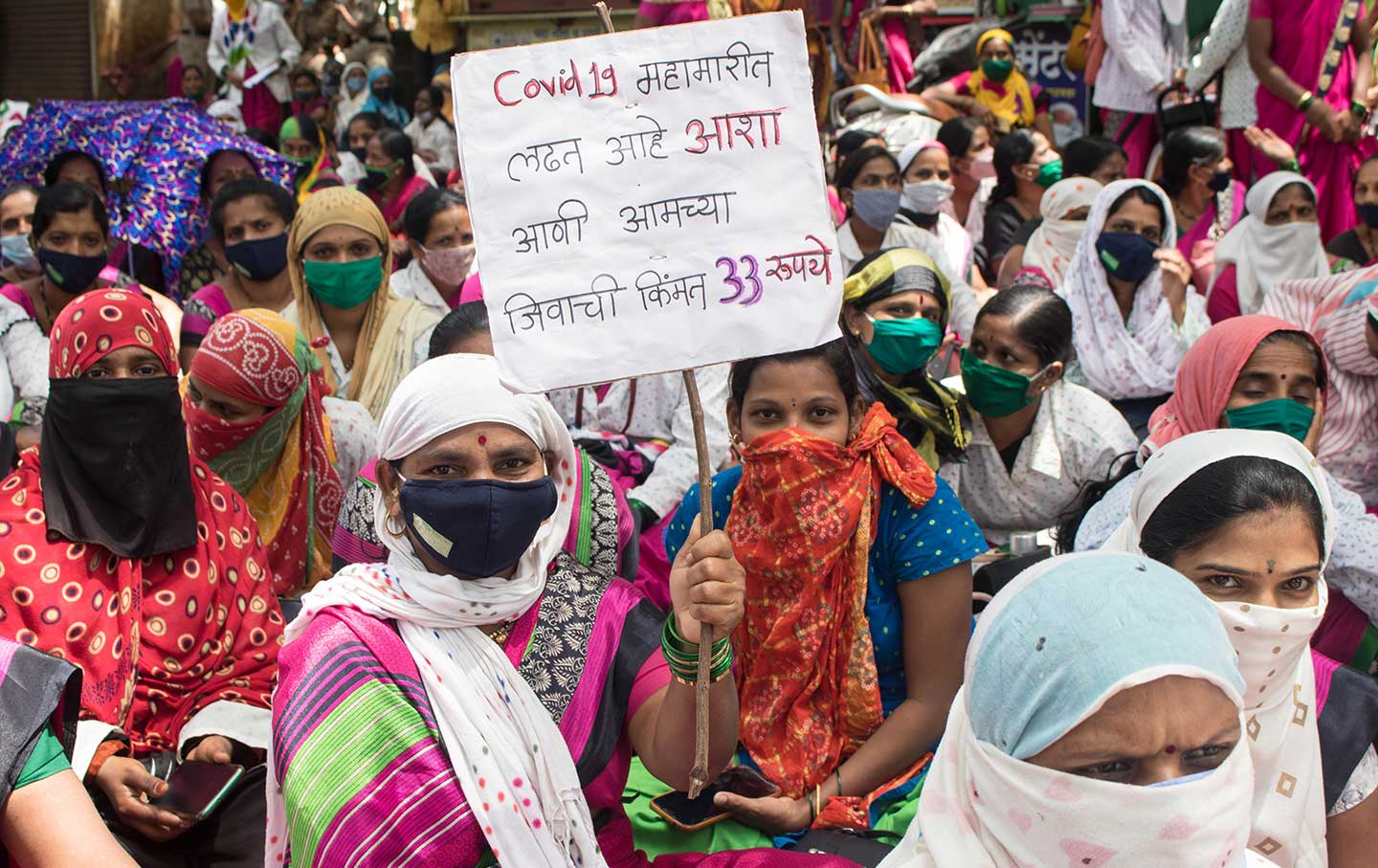 ASHAs hold a sign protesting low pay.