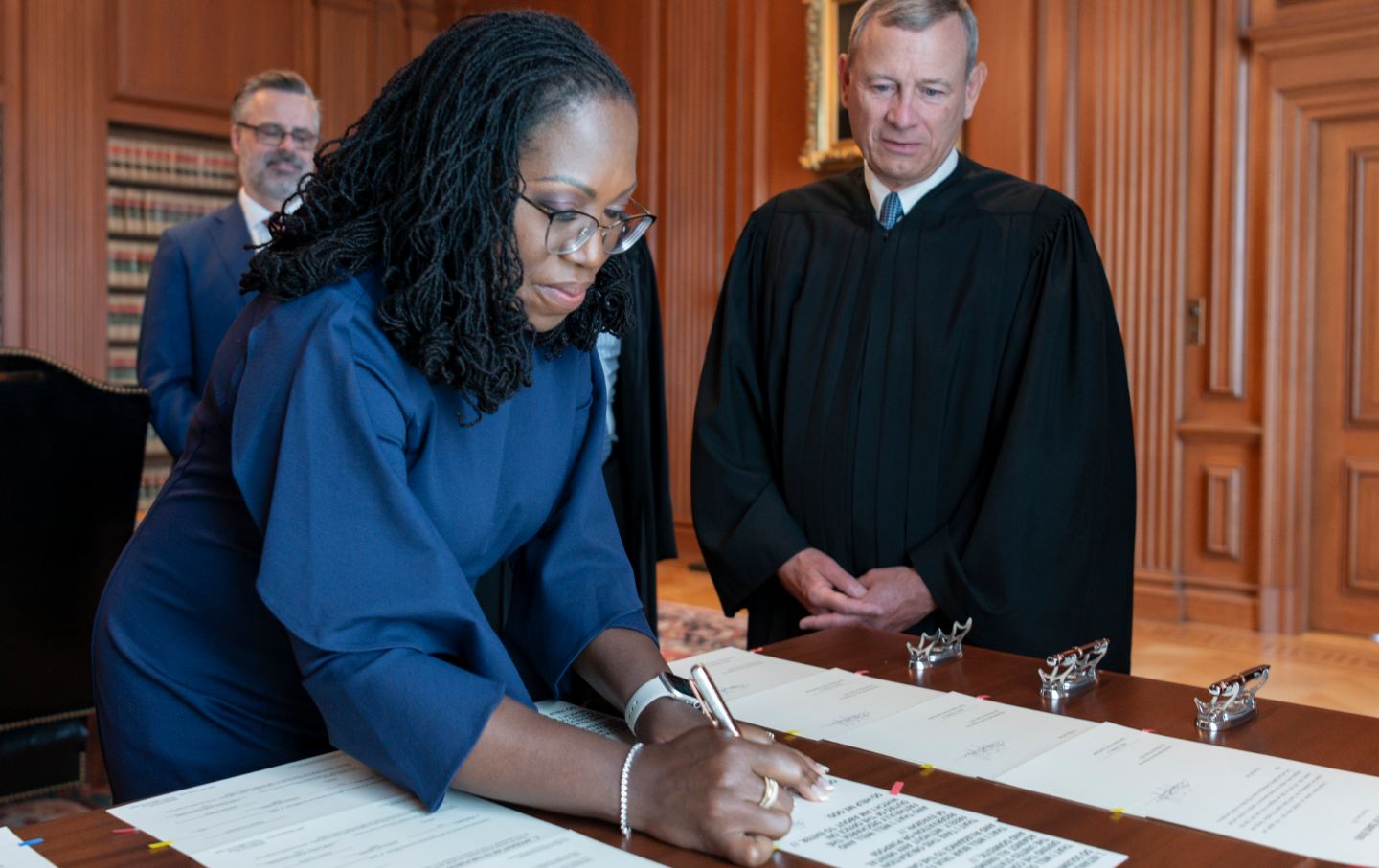A woman signs a document as a man in judicial robes watches.
