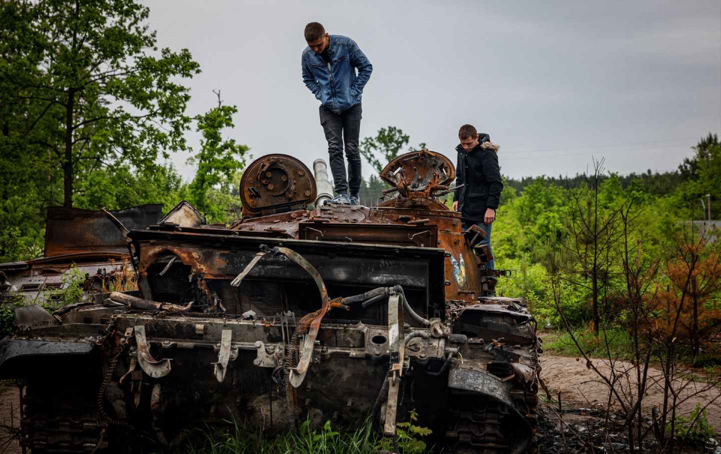 Outside Kyiv, Ukraine, locals stand atop and examine a destroyed Russian tank.