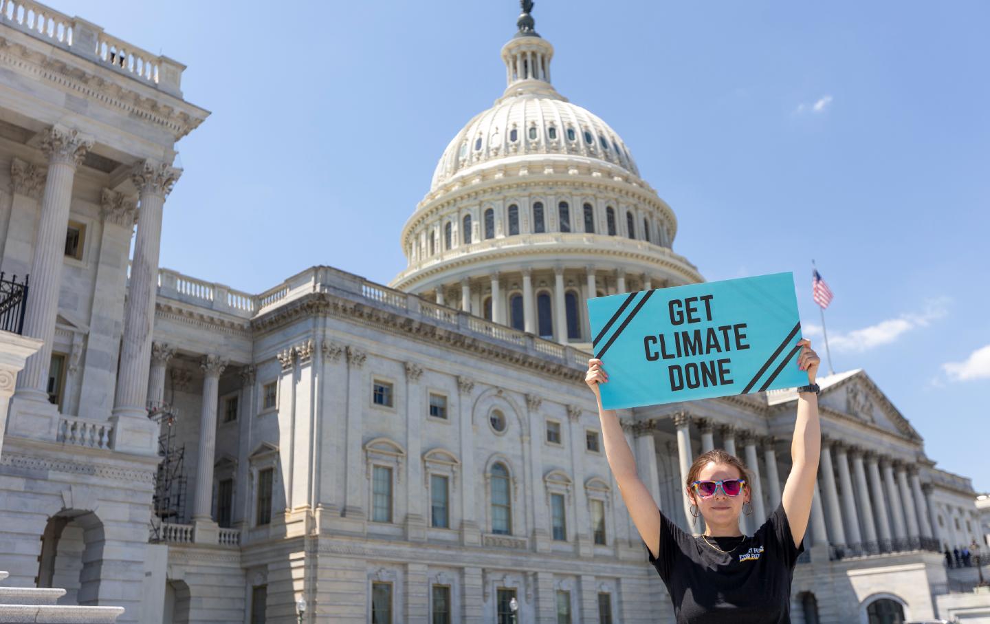 A climate activist holds up a blue placard reading 