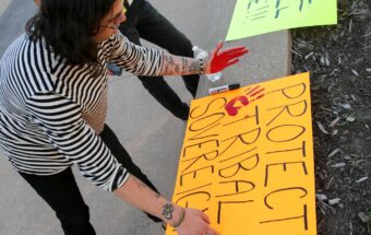 A person applies a red handprint onto a poster that reads 
