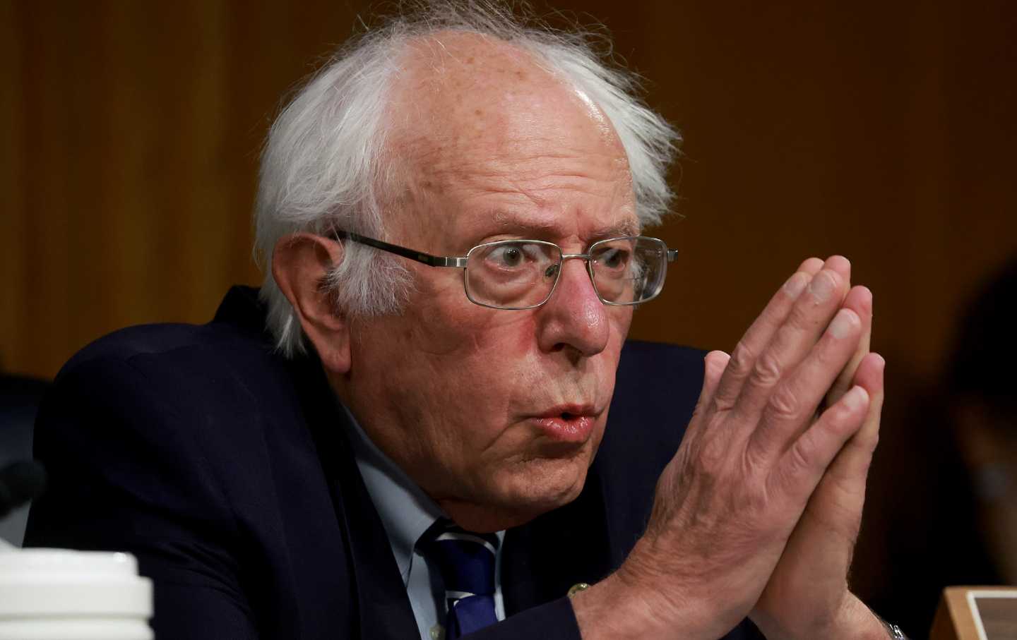 Bernie Sanders speaking with his hands clasped in front of his face.