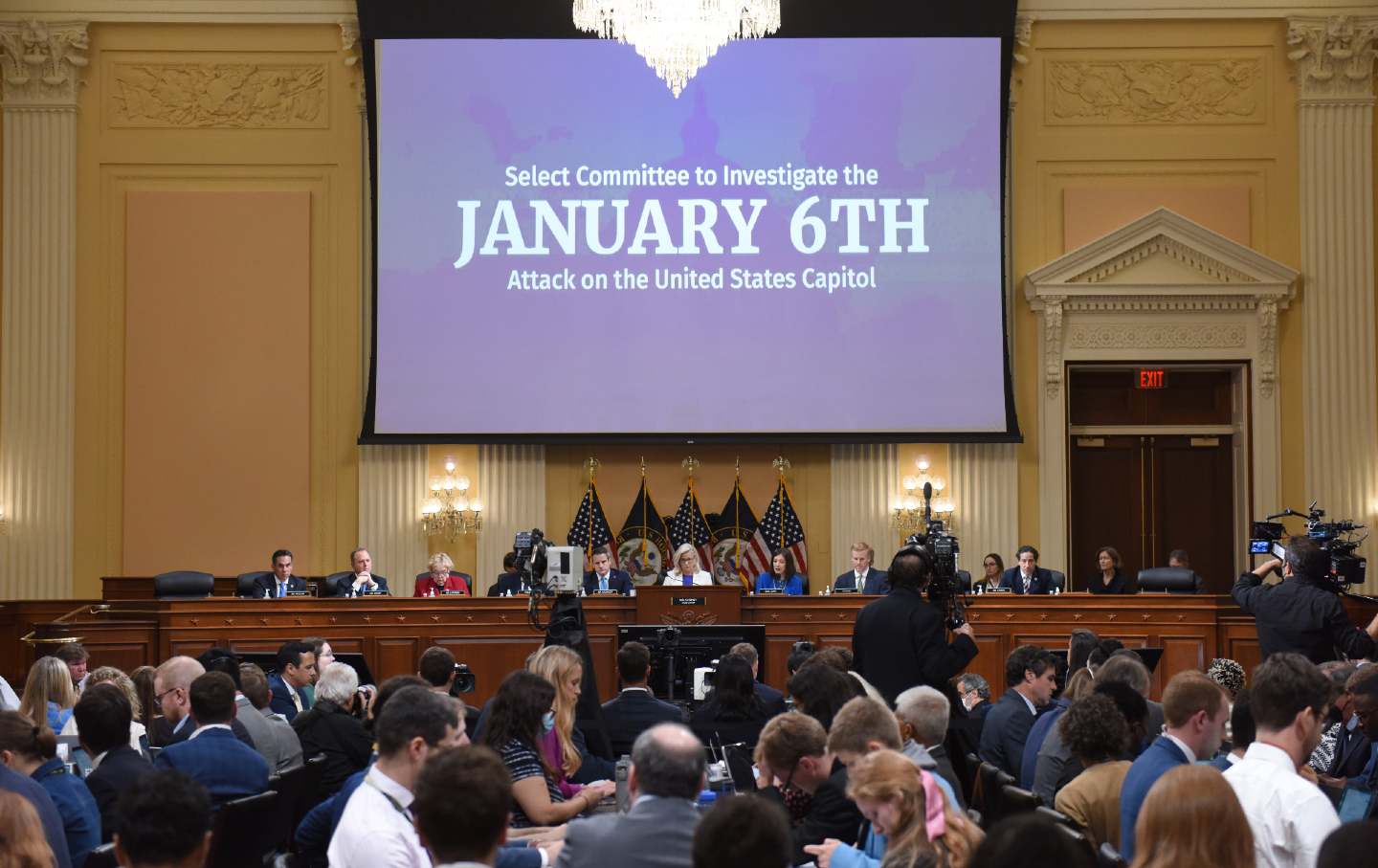 Representative Liz Cheney speaks during the January 6th hearings, under a large screen reading 