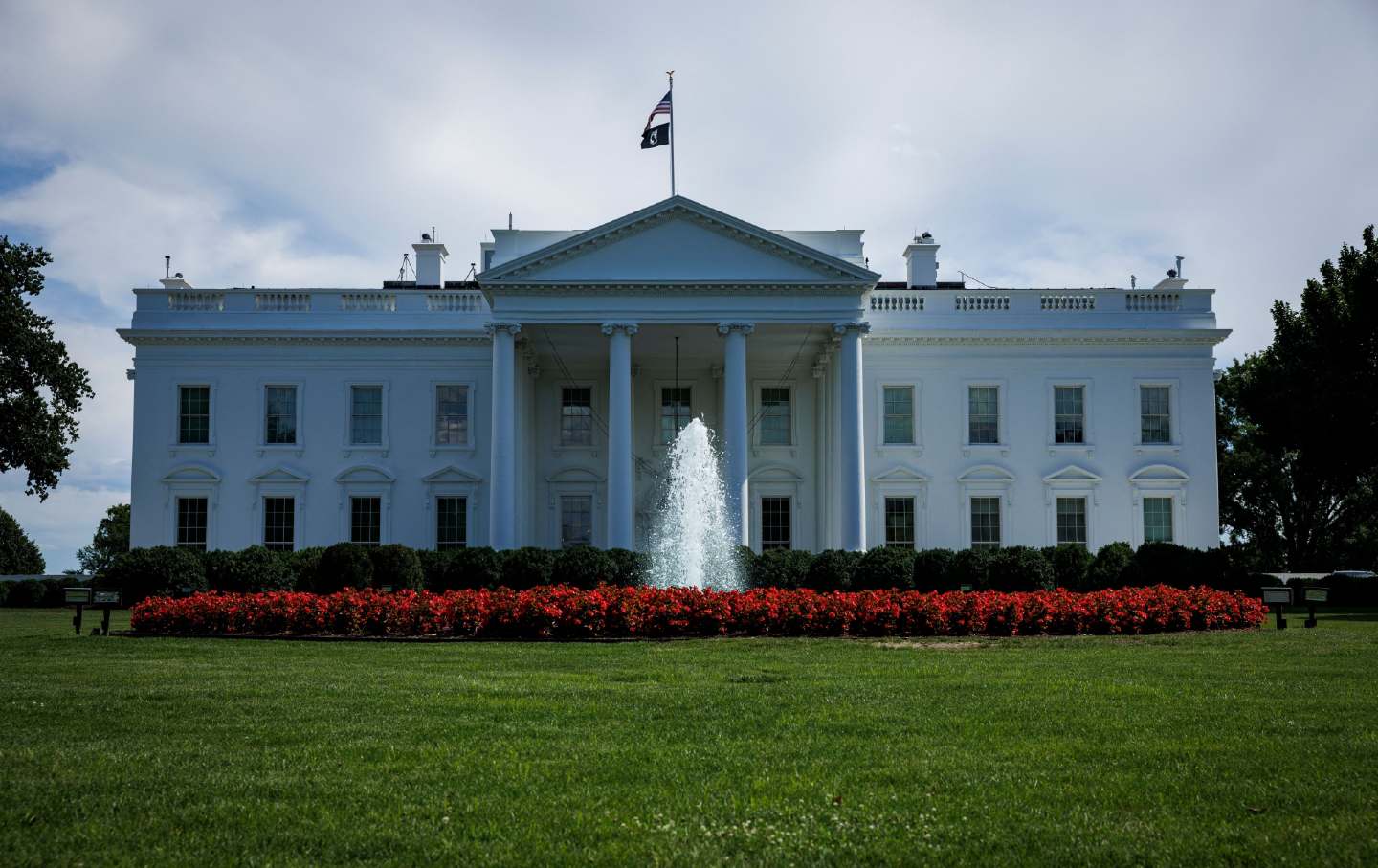 A saturated, dark photo of the White House. The fountain is bright against the red bushes and green grass.