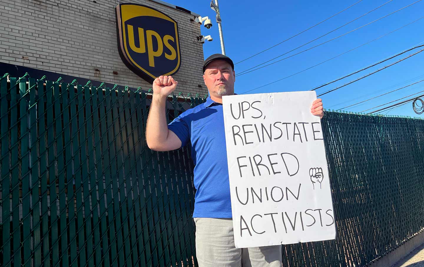 Dan Arlin in a blue polo holds his fist up while holding a sign.