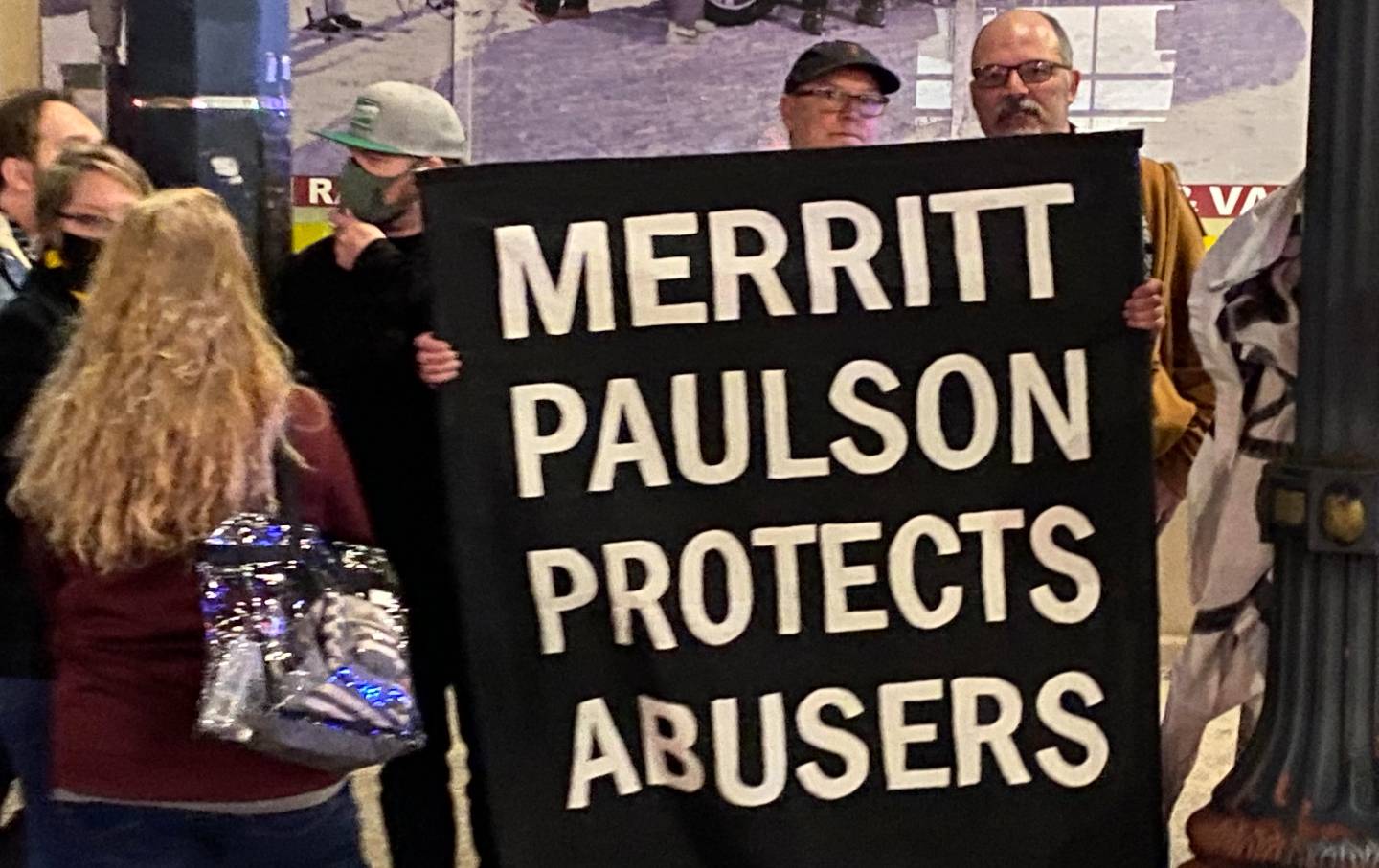 A man holds a black sign with white font that says, 