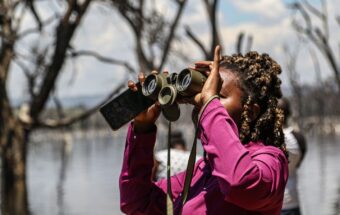 A journalist using binoculars during an event to understand the impact of climate change on biodiversity in Kenya's Lake Nakuru National Park