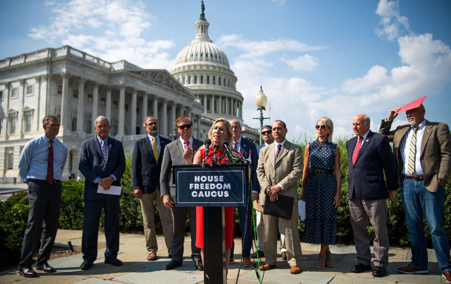Rep. Marjorie Taylor Greene speaking outside the Capitol during a 2021 House Freedom Caucus news conference. From left to right behind her are Reps. Scott Perry, Ralph Norman, Andy Harris, Randy Weber, Dan Bishop, Andrew Clyde, Bob Good, Mary Miller, Louie Gohmert, and Chip Roy.