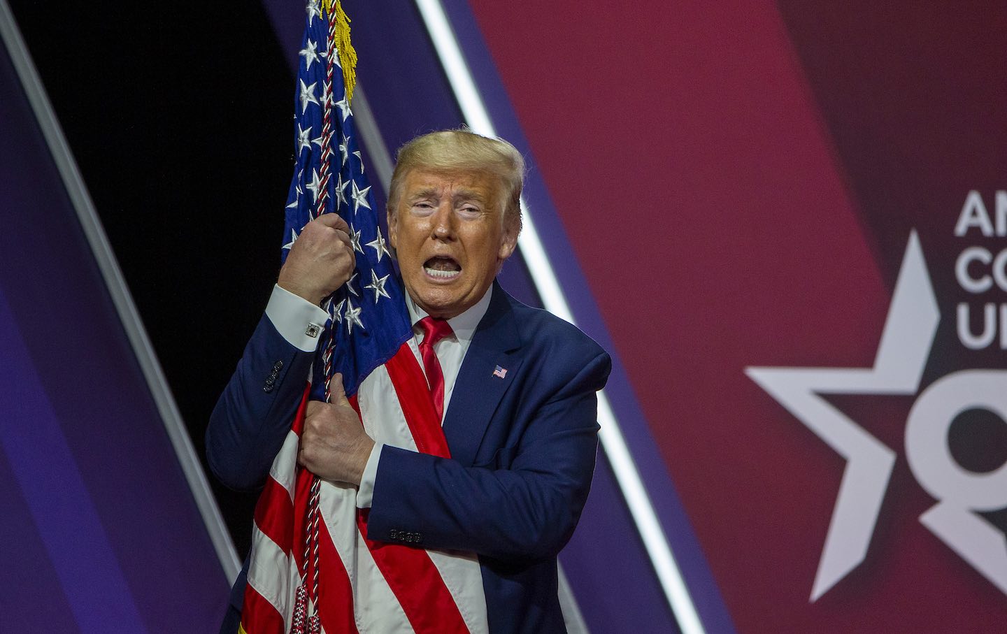 Donald Trump hugs the flag of the United States of America at the annual Conservative Political Action Conference in 2020.