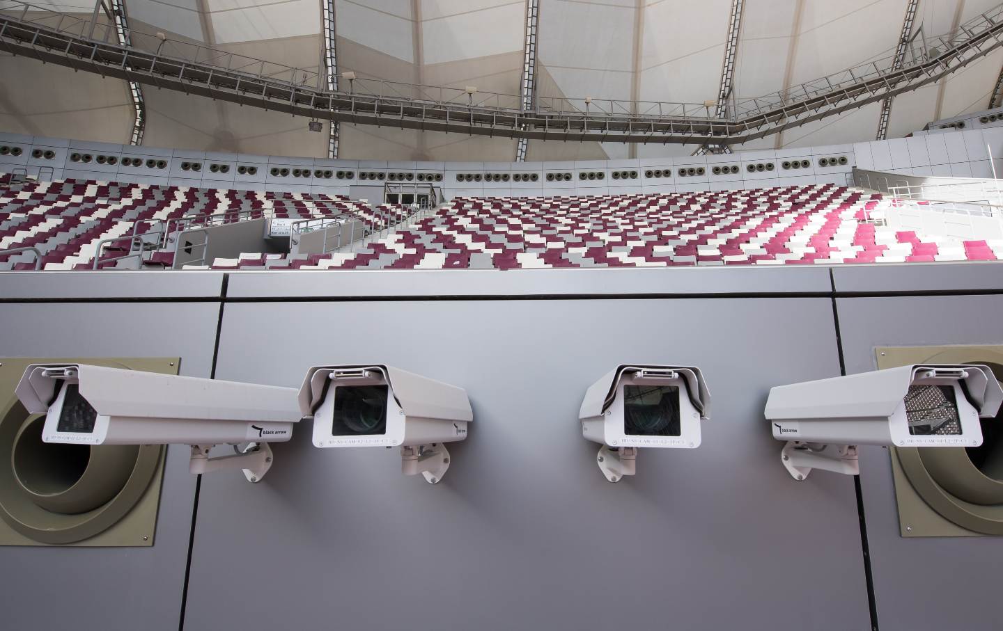 Four surveillance cameras hang inside a stadium.