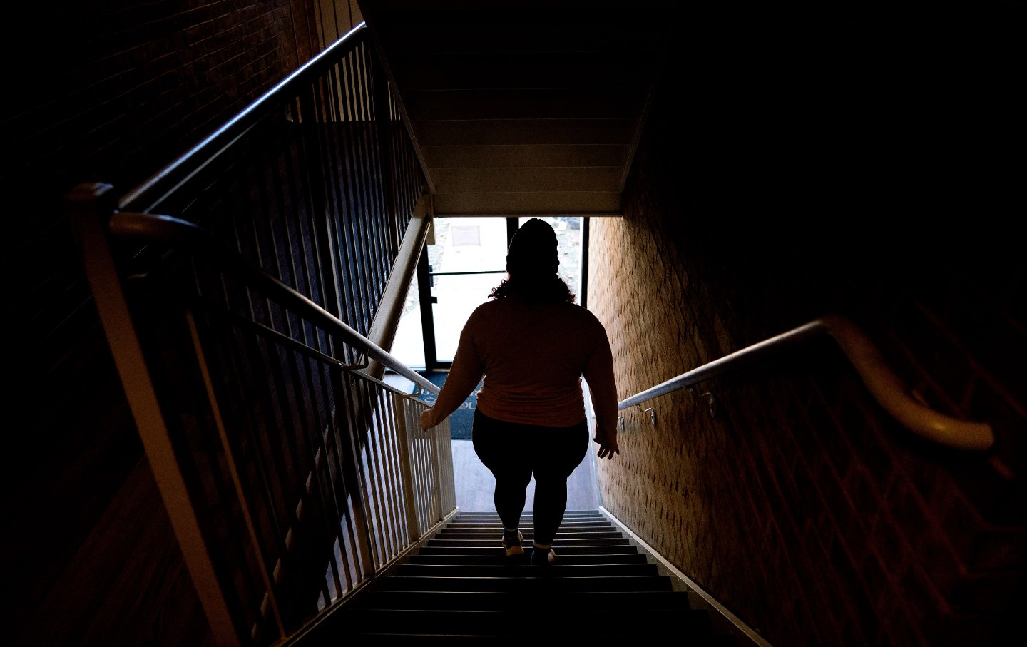 A woman, seen in silhouette, works down a staircase in a home.