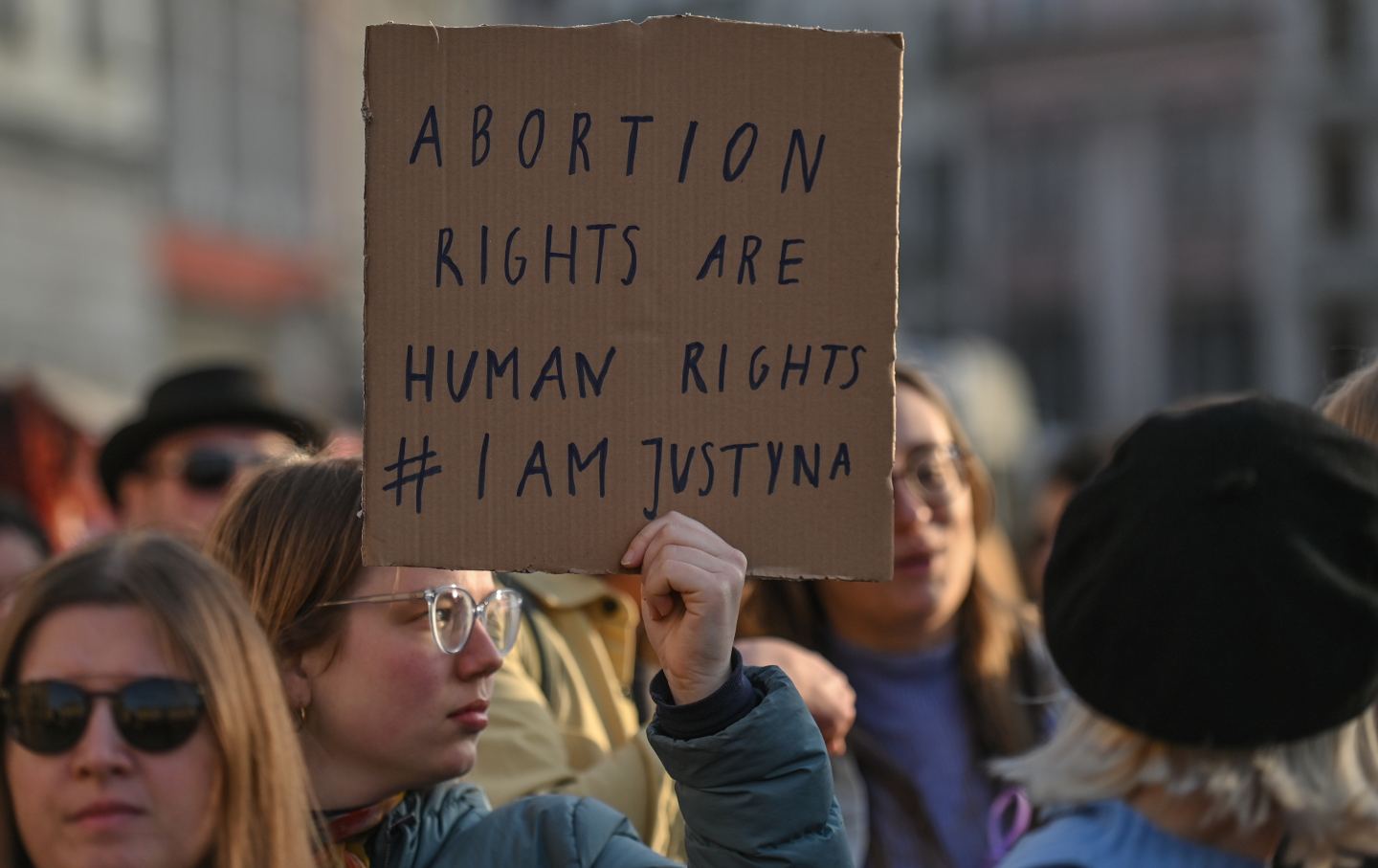 A woman in a crowd holds a sign reading 