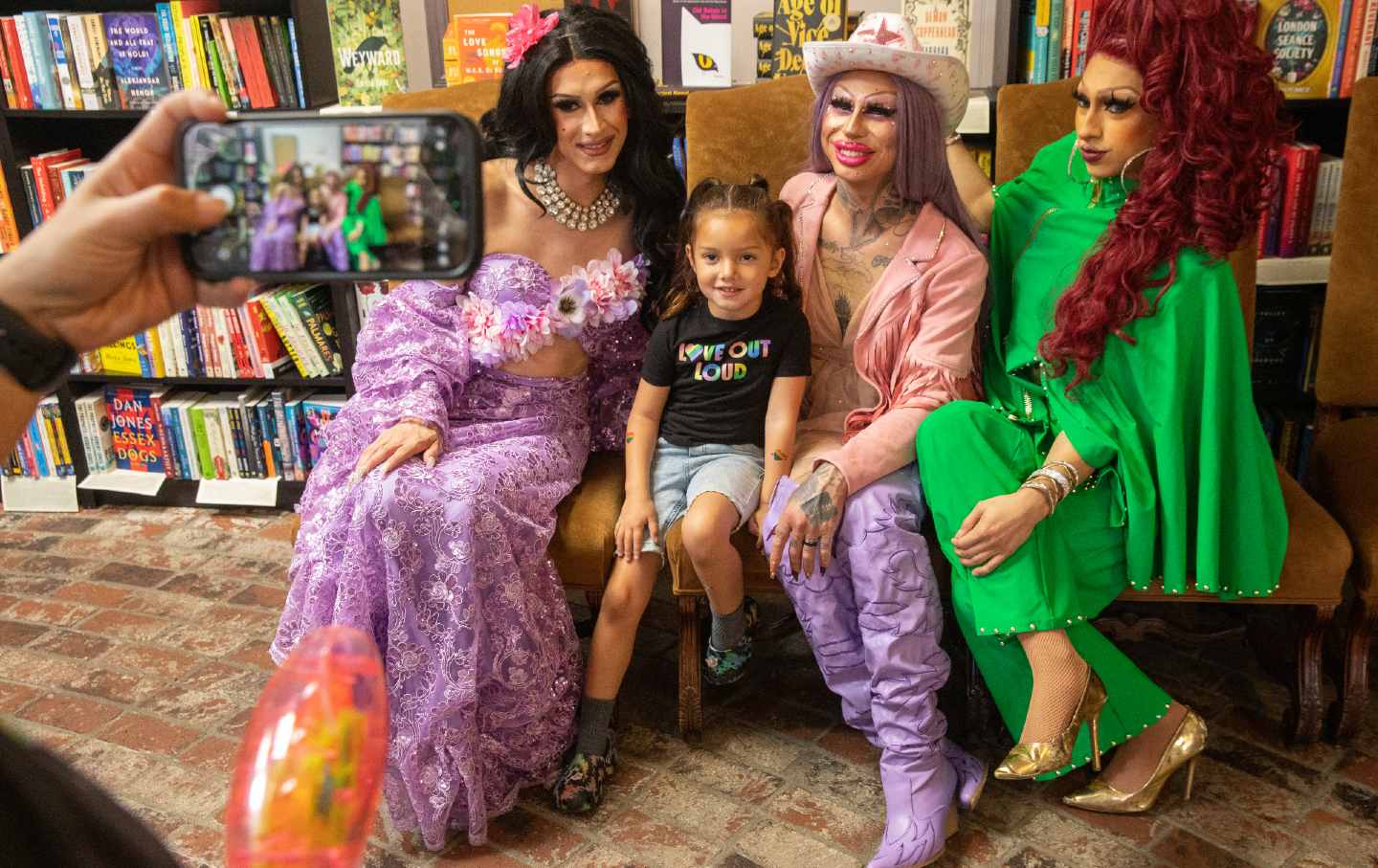 Jennyvieve Barquero-Hughes, 4, in black, gets her photo taken with Drag Queens Kelly K, left, Scalene OnixXx and Athena Monet Kills at the Drag Queen story hour at the Cellar Door Bookstore on Saturday, April 29, 2023 in Riverside, Calif.