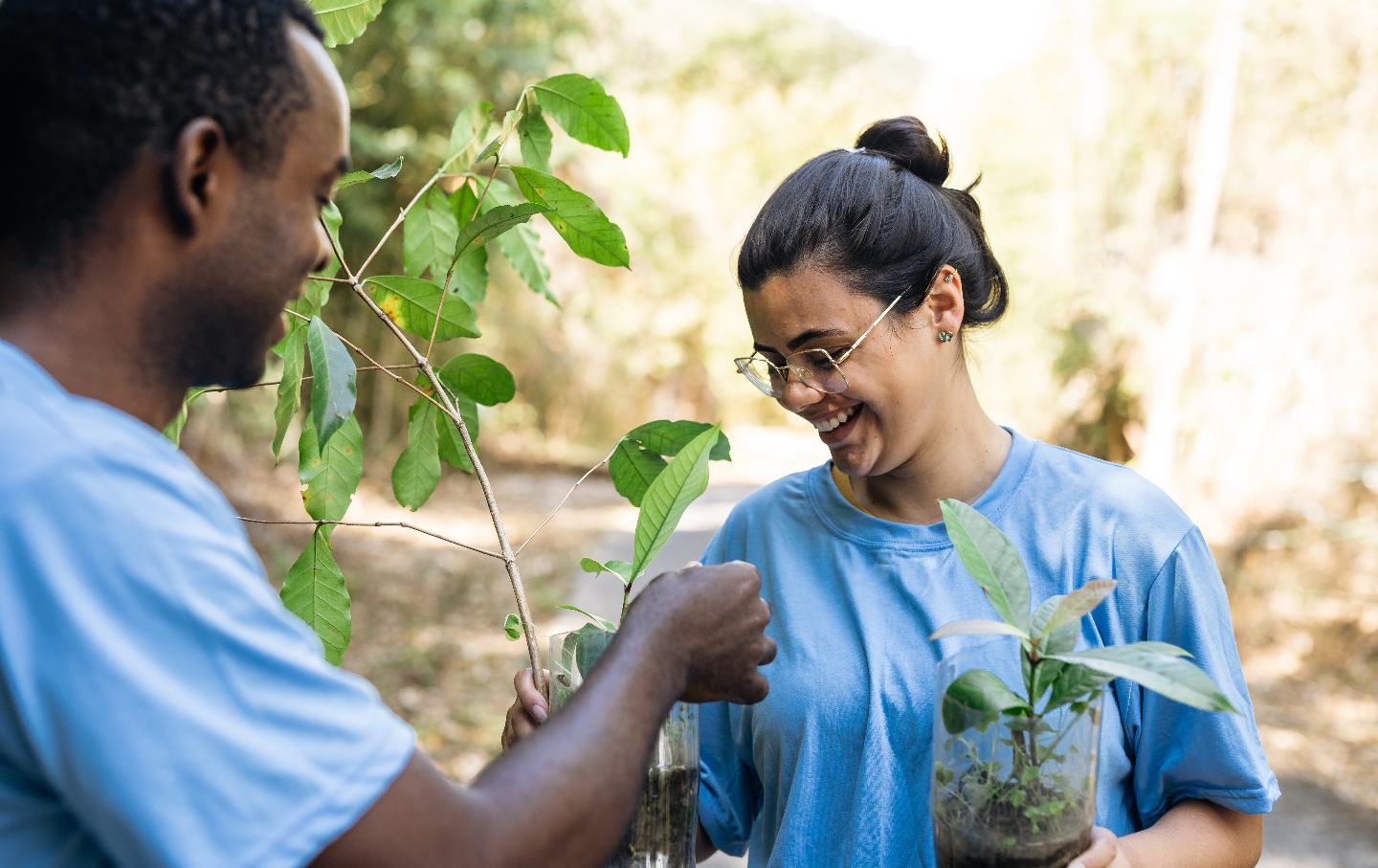 Two people holding tree seedlings for planting.