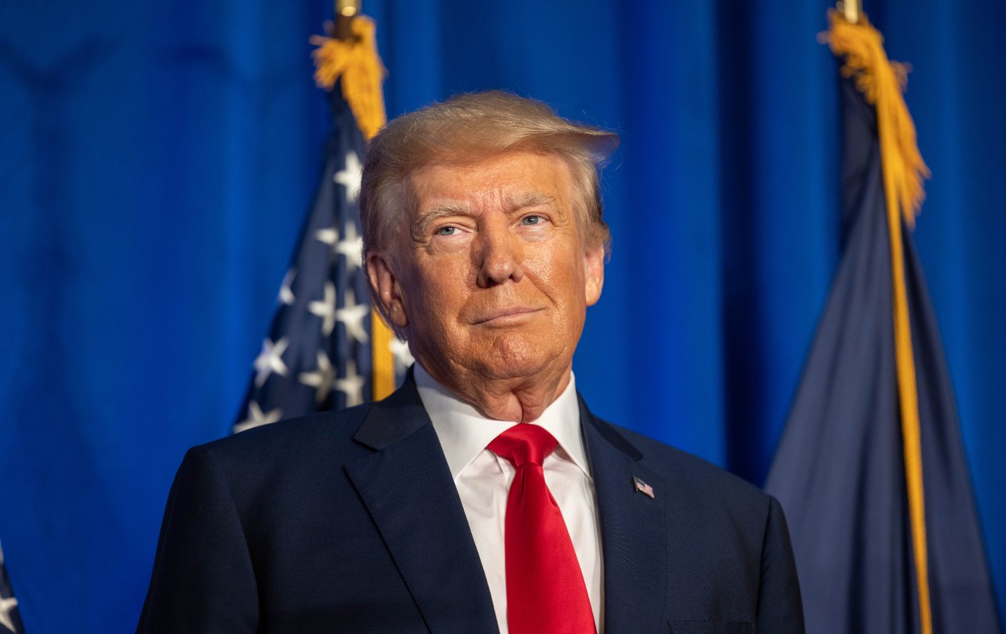 Donald Trump speaking in front of an American flag.