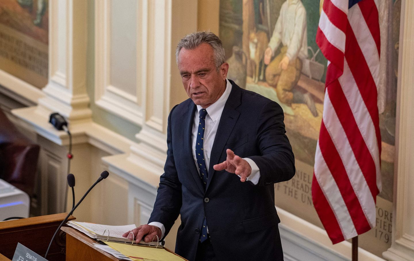 Robert F. Kennedy Jr. speaking at a podium next to an American flag.