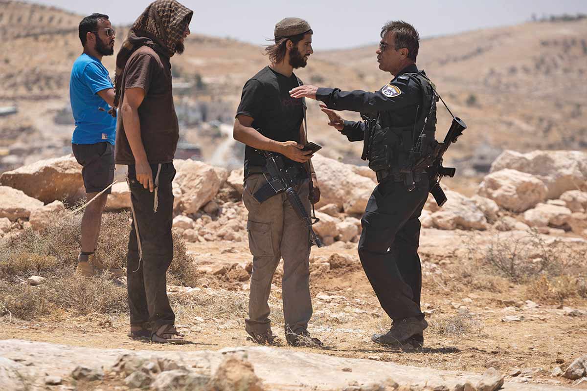 Armed Israeli settlers stand near a policeman during a protest by Palestinians in Masafer Yatta.