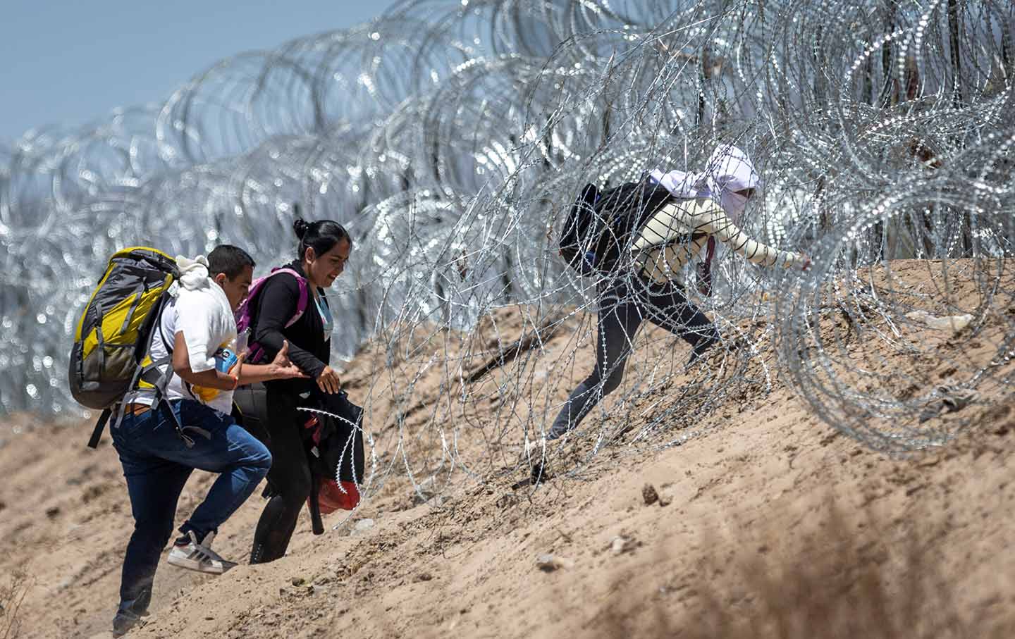 Immigrants walk through razor wire surrounding a makeshift migrant camp after crossing the border from Mexico on May 11, 2023 in El Paso, Texas.