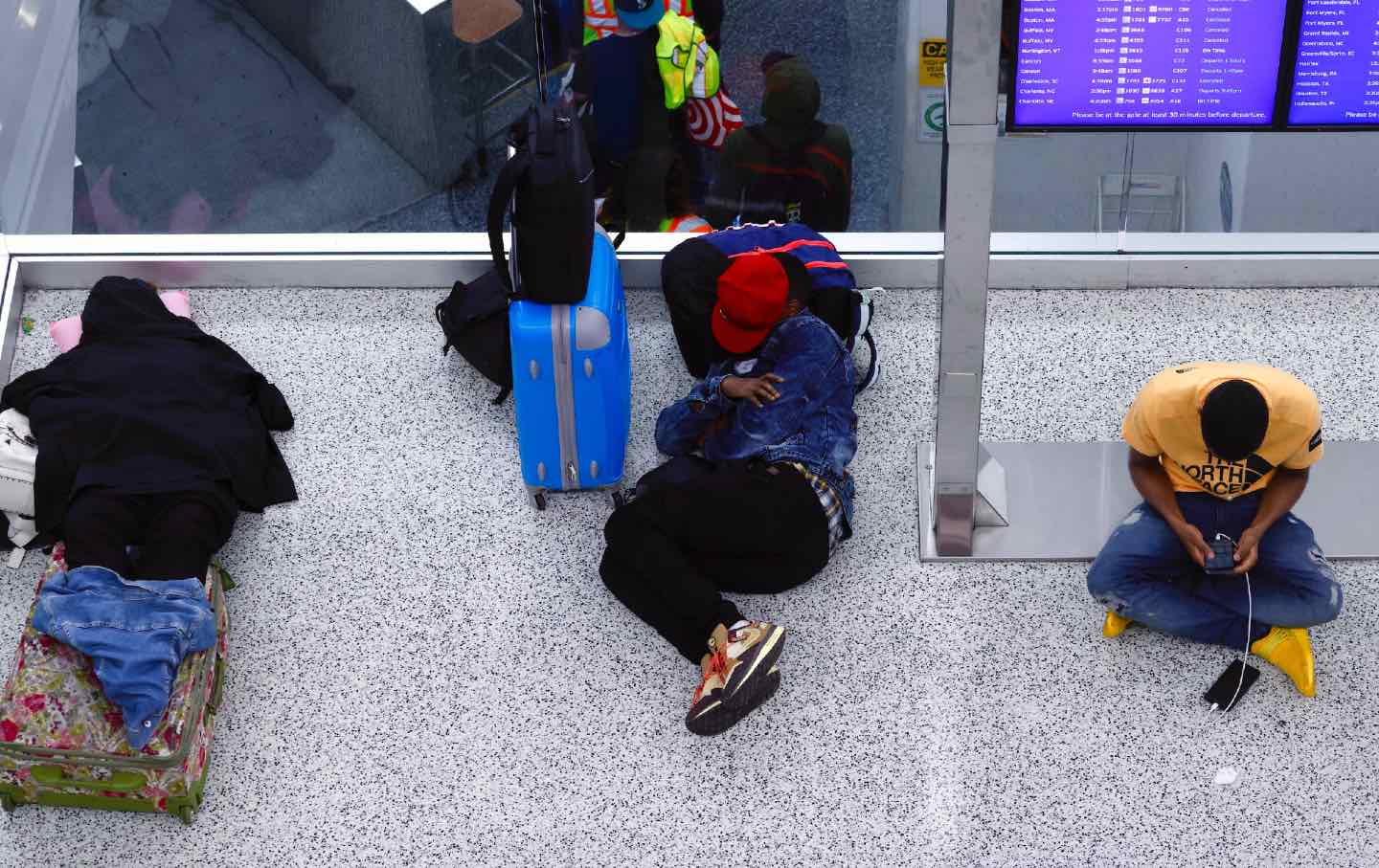 People sit, lay on the ground at the airport with suitcases as they wait for their flights to be rescheduled