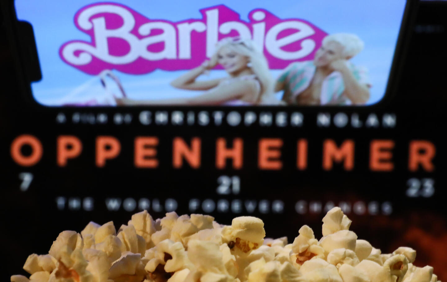 A bag of popcorn, Barbie website displayed on a phone screen and Oppenheimer poster displayed on a screen in the background are seen in this illustration photo taken on August 1, 2023.