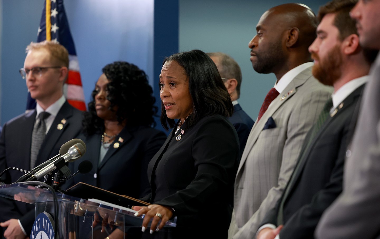 Fani Willis at center, at a podium, flanked by her colleagues.