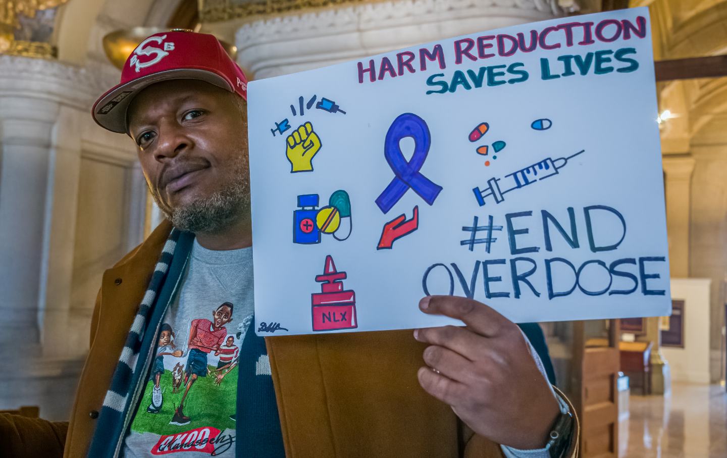 A Black man holds a sign reading, 