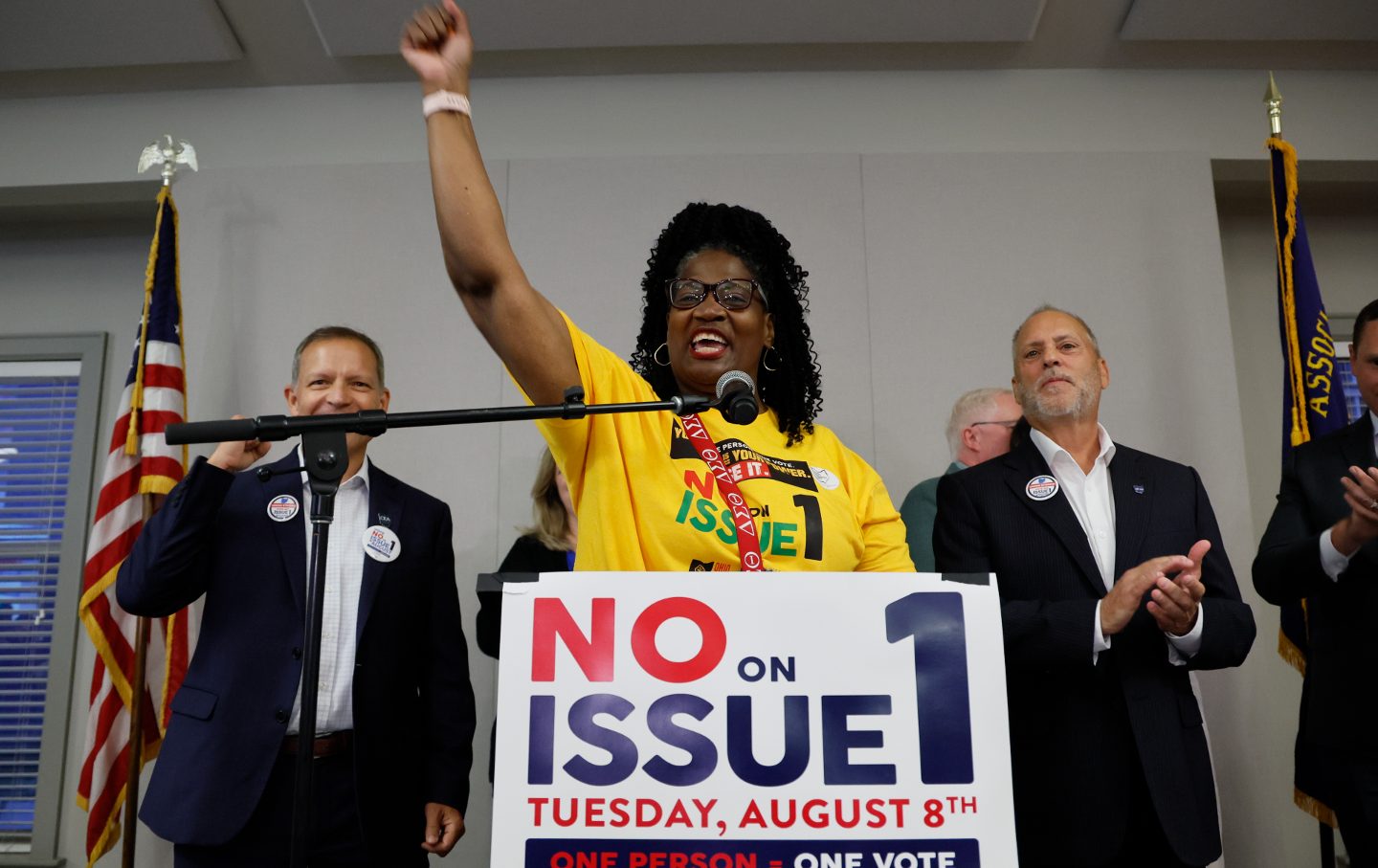 Diedra Reese at a podium with a sign reading "No on Issue 1," lifting her fist in the air in celebration.