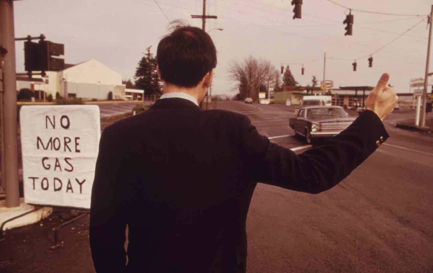 A businessman hitchhiking at a gas station in Oregon, 1973.
