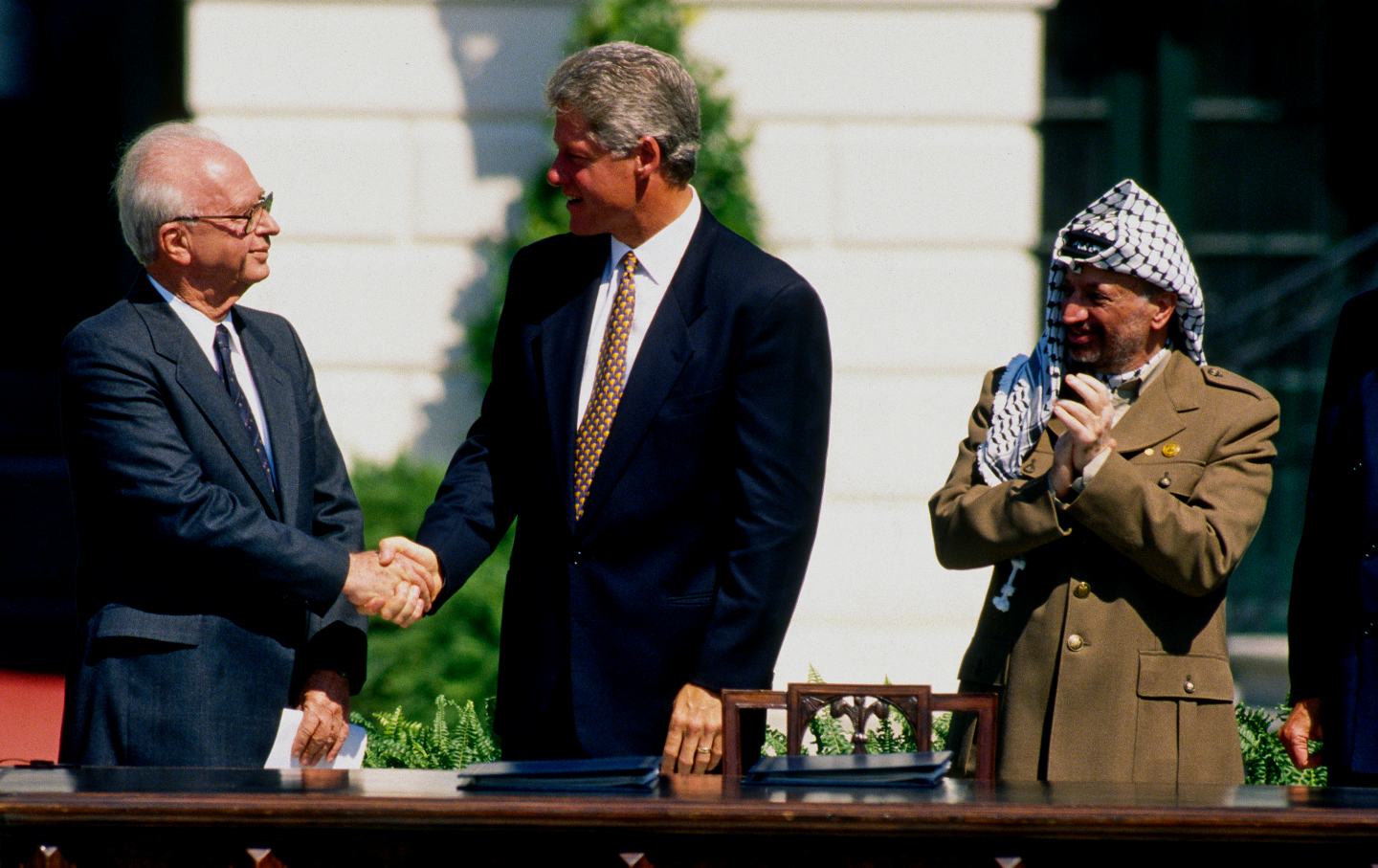Palestine Liberation Organization (PLO) Chairman Yasser Arafat applauds Israeli Prime Minister Yitzhak Rabin and US President Bill Clinton at the signing of the Oslo I Accord on the White House's South Lawn, Washington DC, September 13, 1993.