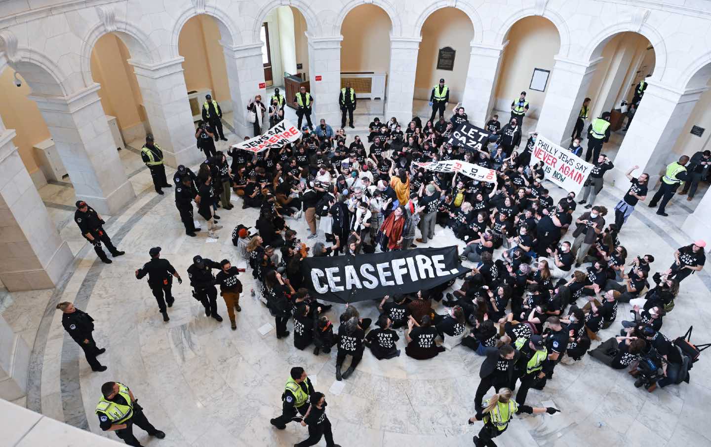 protesters wear shirts reading "not in our name", and hold posters that read "ceasefire," and "jews say never again"; demand ceasefire of Israel's bombing of Palestine