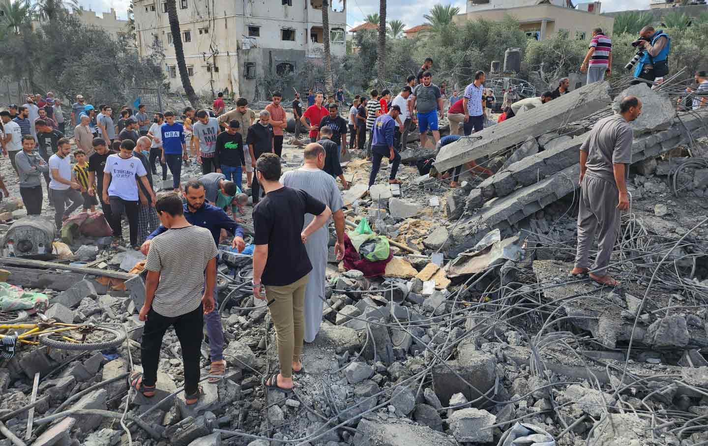 A group of Palestinians stands amid the rubble of a bombed building.