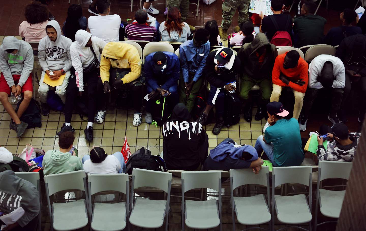 A photo from above of migrants sitting in chairs at Port Authority bus terminal in New York City.