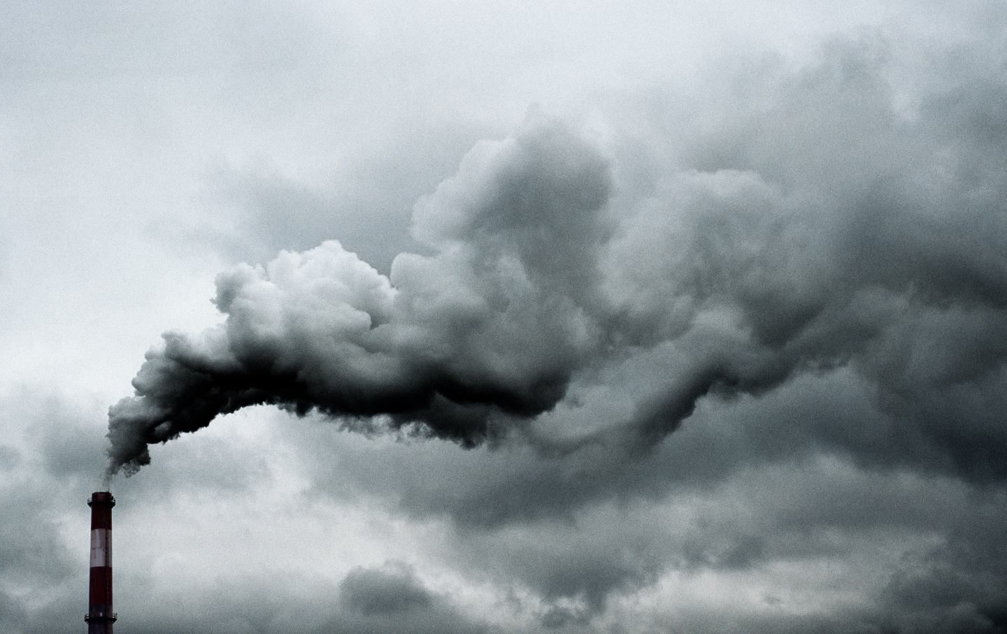 A black-and-white photo of a smokestack billowing out smoke.