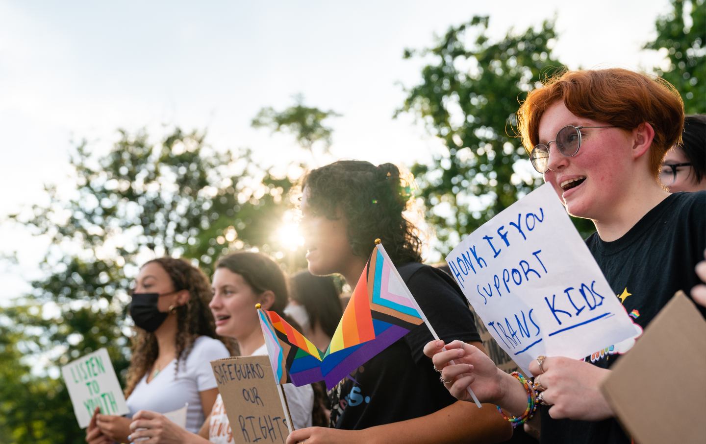 Students hold rainbow LGBTQ flags and a sign saying 