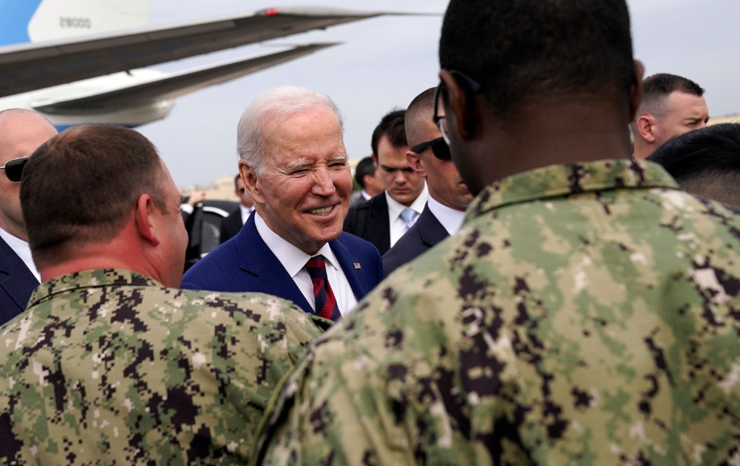 Biden smiling, surrounded by military March 2023