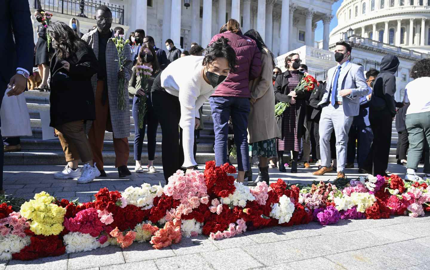 Une personne en pull blanc et masque dépose des roses en ligne