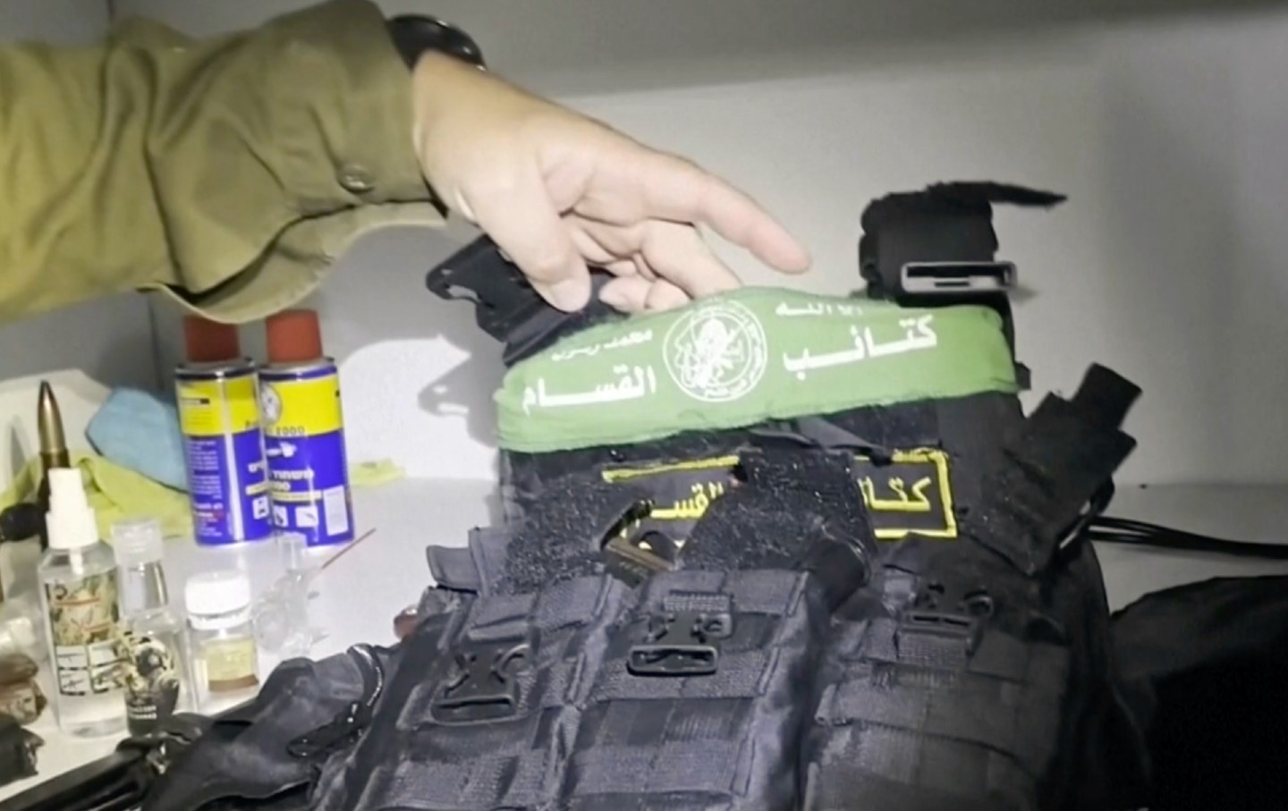 An arm wearing a green shirt holds up a bulletproof vest with a Hamas insignia